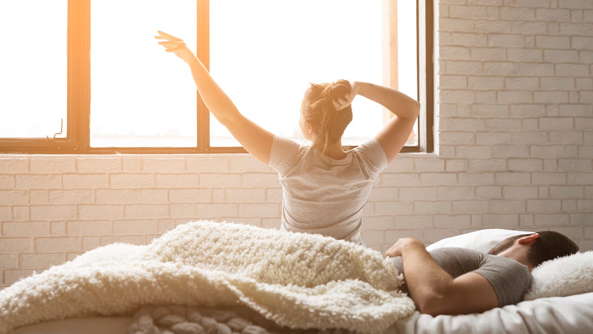 Femme dans un lit lumineux au réveil, évoquant un réveil matinal et le rythme naturel