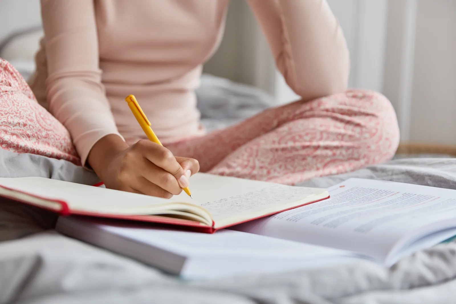 Femme assise dans son lit le soir, écrivant dans un carnet pour apaiser son mental avant de dormir