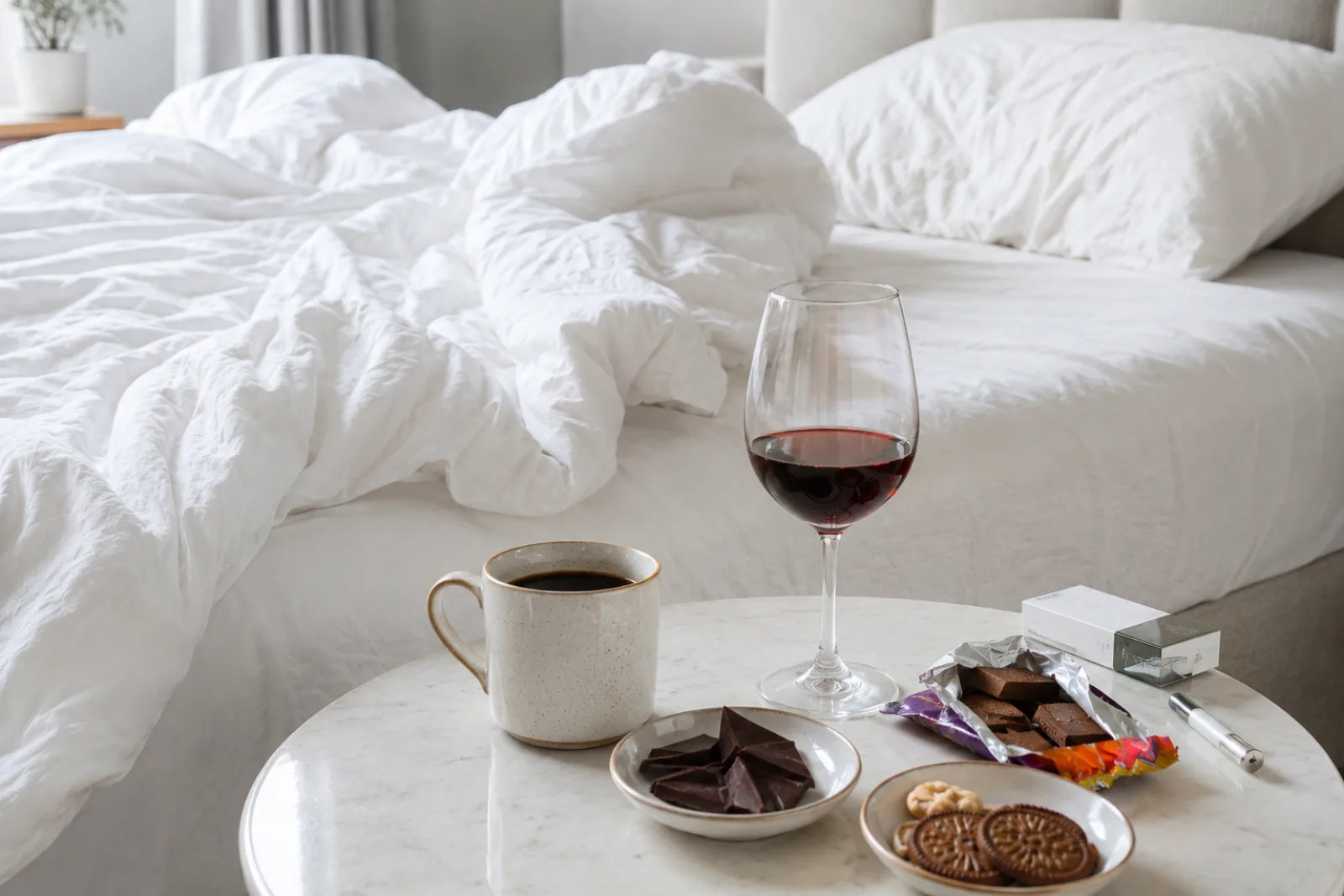 Lit défait avec café, chocolat, verre de vin et encas sucrés, évoquant les aliments et stimulants qui peuvent perturber le sommeil